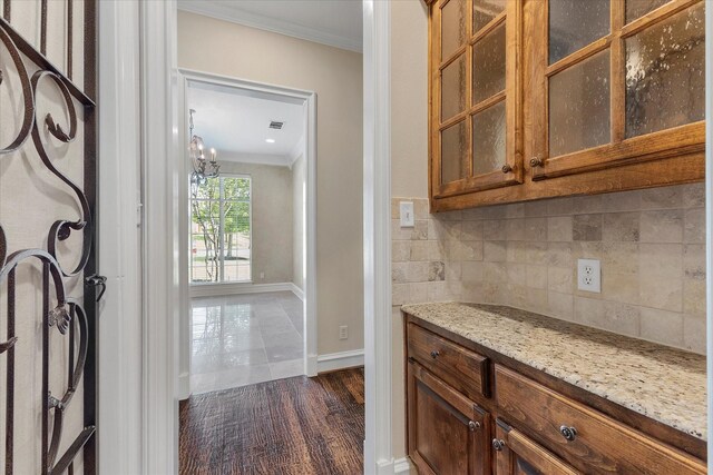 bar featuring crown molding, baseboards, backsplash, and a notable chandelier
