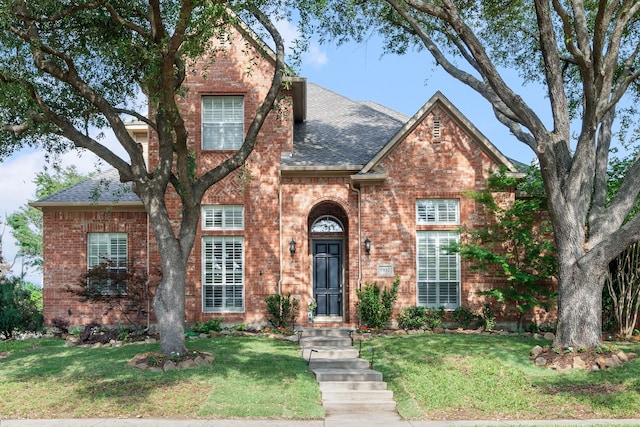 traditional home featuring brick siding, a shingled roof, and a front yard