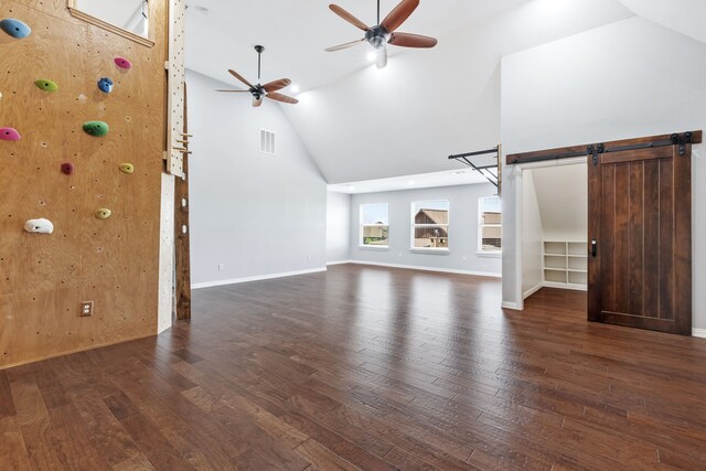 unfurnished living room with ceiling fan, a barn door, wood-type flooring, high vaulted ceiling, and visible vents