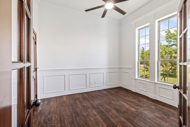 empty room featuring ornamental molding, dark wood-style flooring, wainscoting, a decorative wall, and a ceiling fan