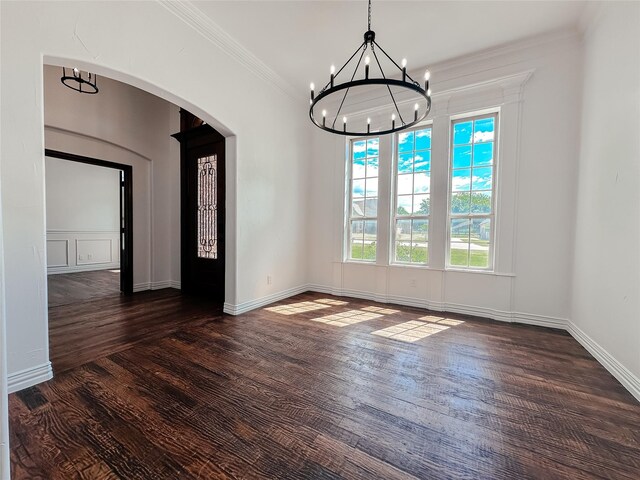 unfurnished dining area with an inviting chandelier, crown molding, baseboards, dark wood-type flooring, and arched walkways