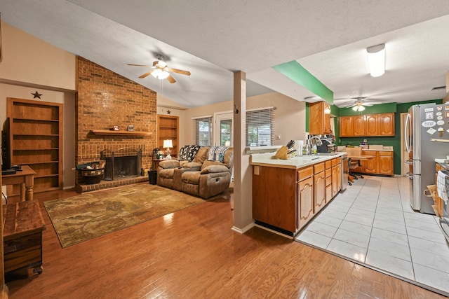 2609 Kimberly Dr, Garland, TX 75040 - kitchen with light countertops, a brick fireplace, freestanding refrigerator, a ceiling fan, and light wood-type flooring