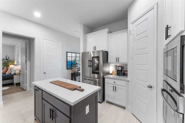 kitchen with a kitchen island, appliances with stainless steel finishes, light countertops, light wood-style floors, and white cabinetry