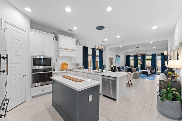 kitchen featuring visible vents, a center island, light countertops, a peninsula, and stainless steel appliances