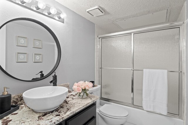 bathroom with vanity, enclosed tub / shower combo, toilet, and a textured ceiling