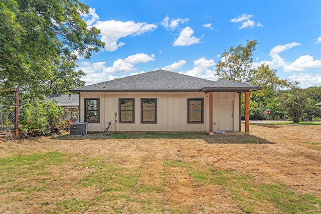 rear view of house with a shingled roof, board and batten siding, a yard, and cooling unit