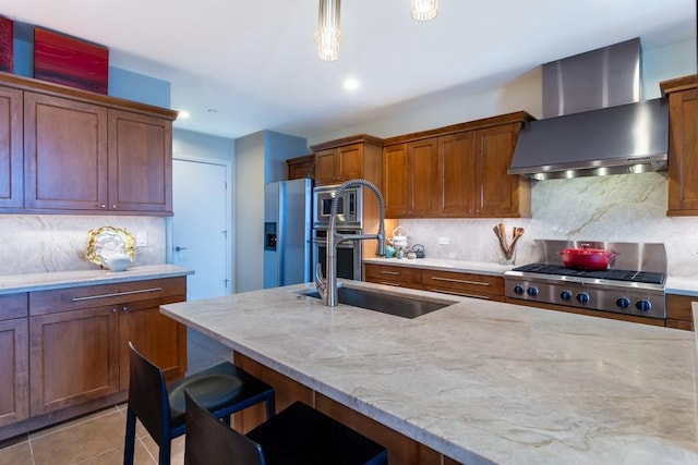 kitchen featuring wall chimney range hood, appliances with stainless steel finishes, light stone counters, a sink, and decorative backsplash