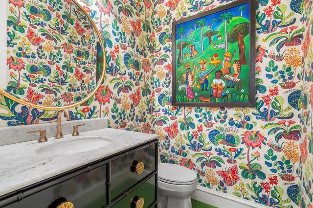 bathroom with vanity, toilet, and wallpapered walls