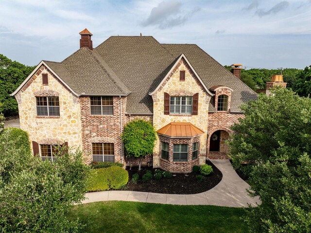 view of front facade with brick siding, a shingled roof, a chimney, and a standing seam roof