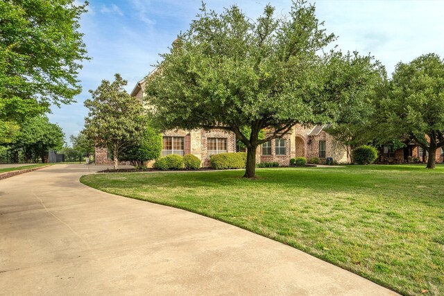 view of property hidden behind natural elements featuring brick siding and a front yard