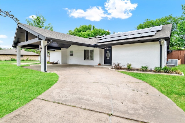 ranch-style home with a front lawn, roof with shingles, an attached carport, driveway, and solar panels