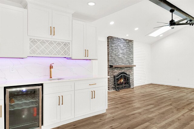 bar with decorative backsplash, beverage cooler, indoor wet bar, light wood-type flooring, and lofted ceiling with beams