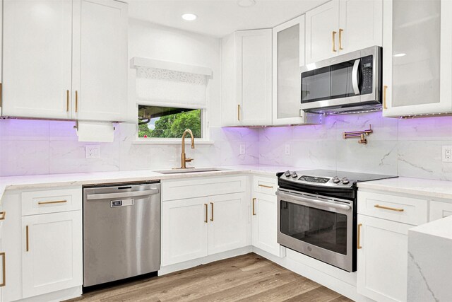 kitchen with glass insert cabinets, white cabinets, light stone counters, a sink, and appliances with stainless steel finishes