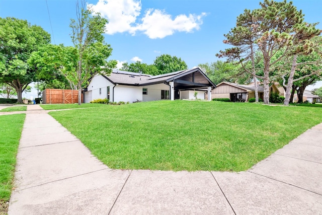 ranch-style home with fence, a gate, roof mounted solar panels, and a front yard
