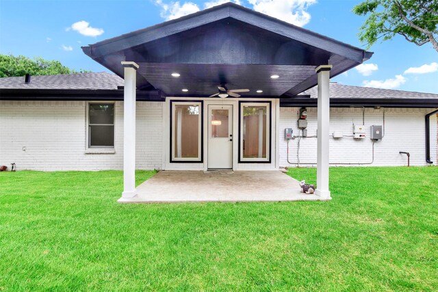 property entrance with ceiling fan, a patio, brick siding, a shingled roof, and a lawn
