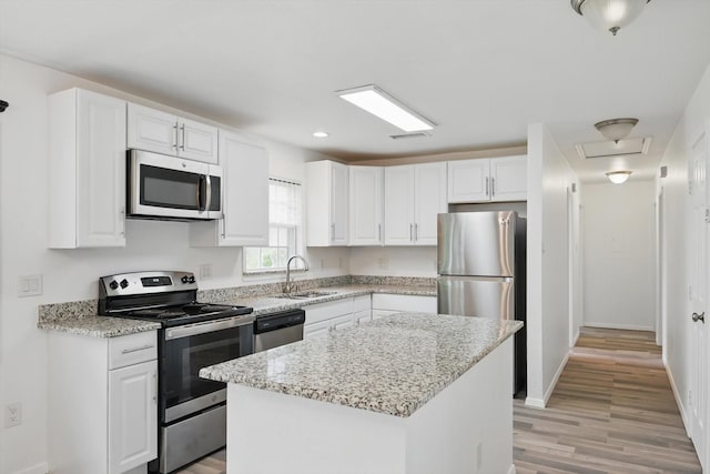kitchen featuring white cabinets, light stone counters, a sink, stainless steel appliances, and light wood-type flooring