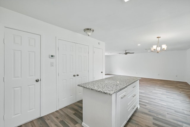 kitchen with hanging light fixtures, light stone counters, ceiling fan with notable chandelier, white cabinetry, and wood finished floors
