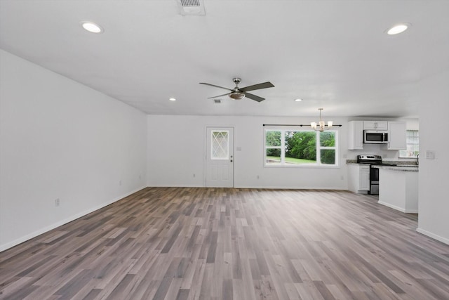 unfurnished living room with light wood-style floors, ceiling fan with notable chandelier, recessed lighting, baseboards, and visible vents
