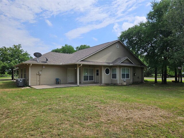 view of front of house featuring a patio, central AC unit, a shingled roof, and a front yard