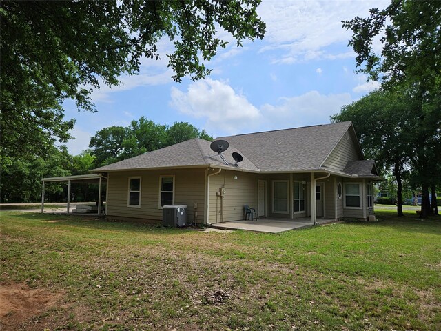rear view of property with central air condition unit, a patio, a yard, and roof with shingles