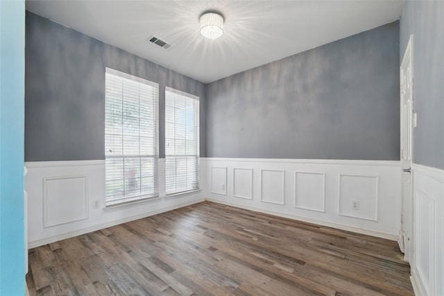 empty room with a decorative wall, visible vents, wood finished floors, and a wainscoted wall