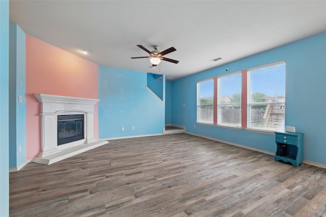 unfurnished living room with a ceiling fan, visible vents, wood finished floors, baseboards, and a glass covered fireplace