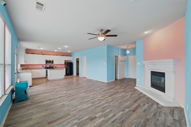 unfurnished living room with ceiling fan, visible vents, a wealth of natural light, and light wood-style floors
