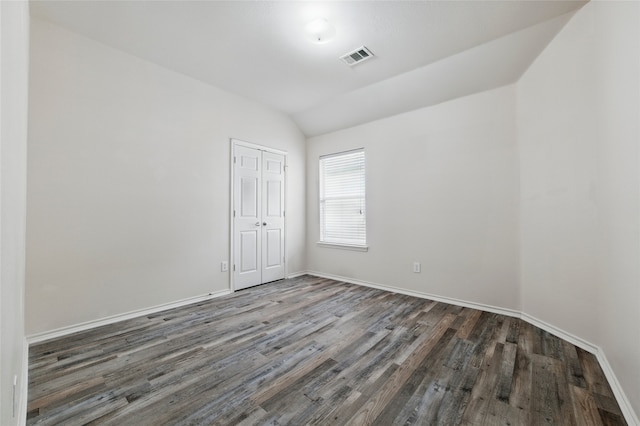 spare room featuring baseboards, vaulted ceiling, wood finished floors, and visible vents