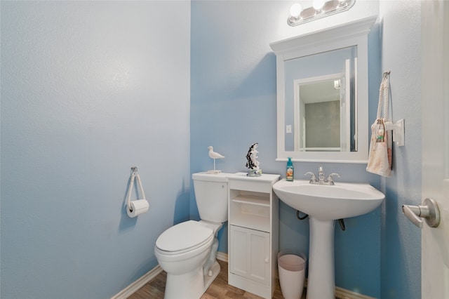 half bath featuring toilet, baseboards, a sink, and wood finished floors
