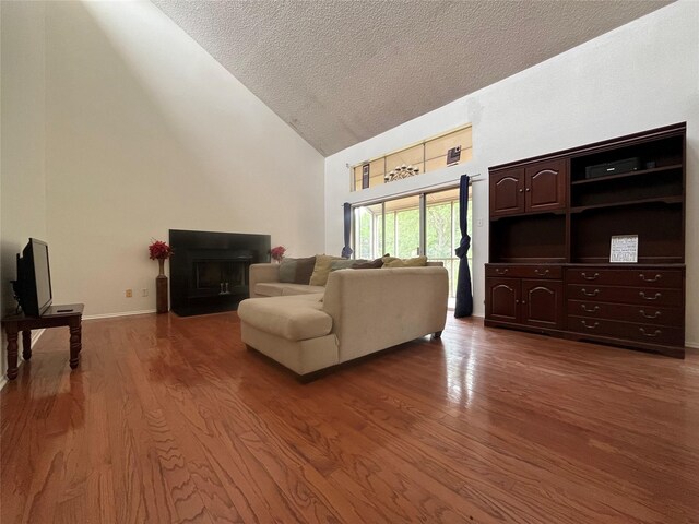 living area featuring a fireplace with flush hearth, a textured ceiling, wood finished floors, and high vaulted ceiling