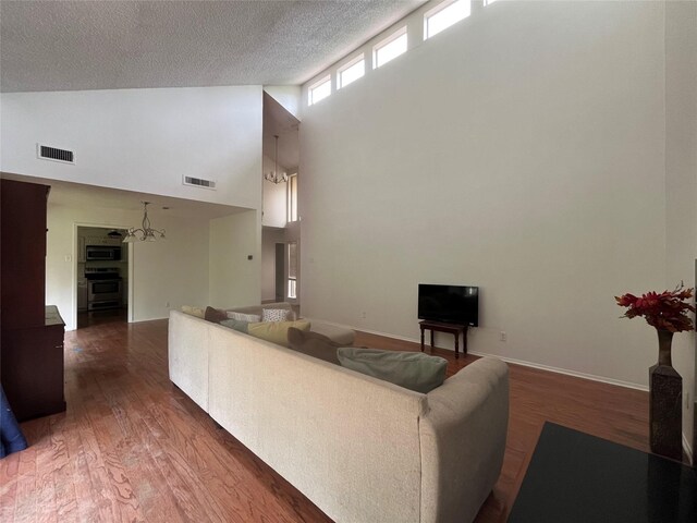 living area featuring visible vents, a textured ceiling, wood finished floors, and high vaulted ceiling