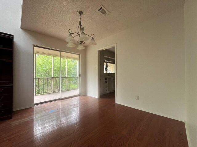 unfurnished dining area featuring wood finished floors, visible vents, a textured ceiling, and a notable chandelier