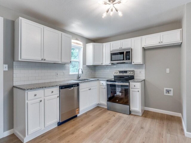 kitchen with appliances with stainless steel finishes, light stone countertops, a sink, baseboards, and white cabinets