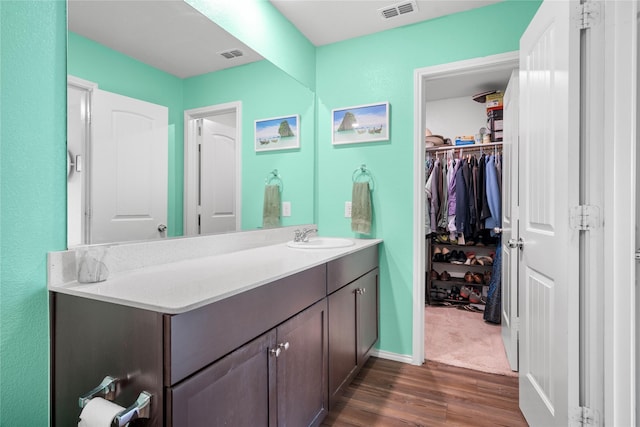 bathroom with vanity, a walk in closet, wood finished floors, and visible vents