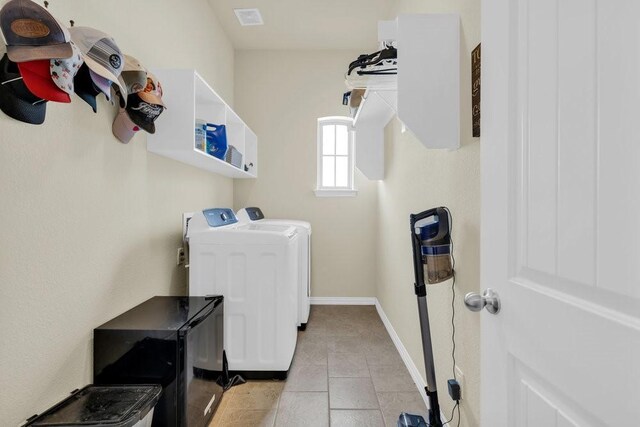 clothes washing area with laundry area, visible vents, light tile patterned floors, baseboards, and washer and clothes dryer