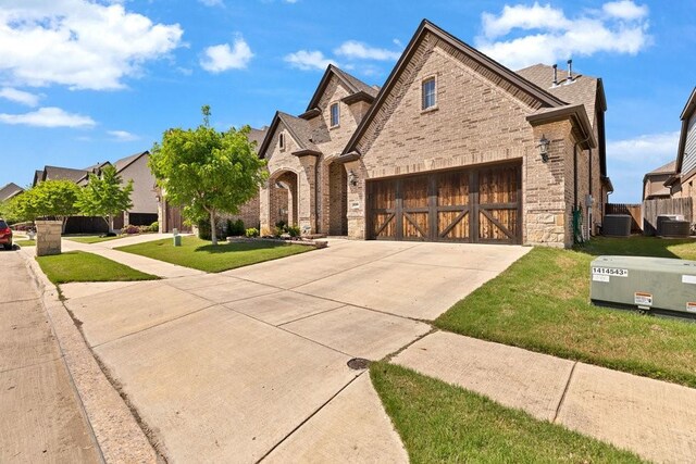 french country inspired facade featuring brick siding, central air condition unit, a front yard, and concrete driveway
