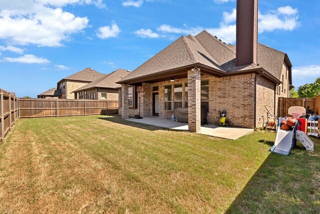 rear view of property with brick siding, a patio, a fenced backyard, and a lawn