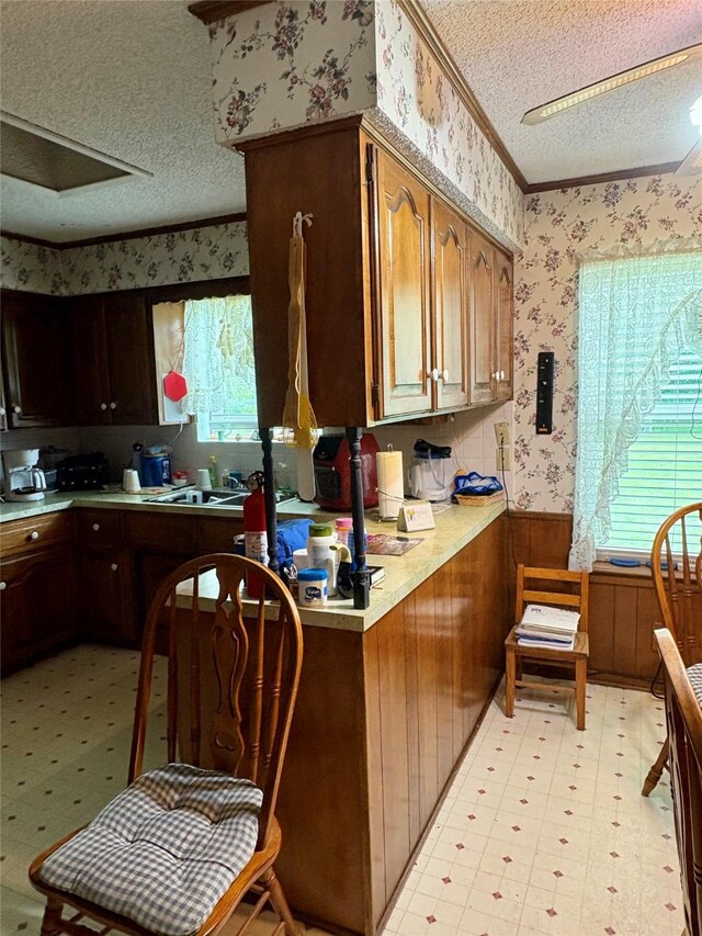 kitchen with a textured ceiling, light countertops, light floors, ornamental molding, and wallpapered walls
