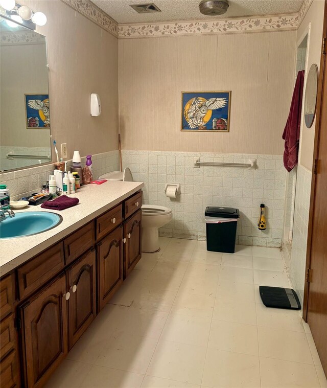bathroom with toilet, tile walls, wainscoting, and vanity