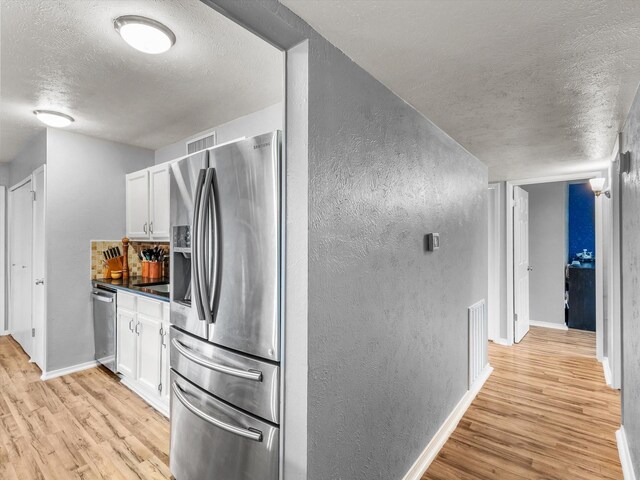 kitchen with a textured wall, light wood finished floors, a textured ceiling, stainless steel appliances, and white cabinetry