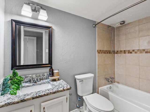 full bath with shower / tub combination, vanity, baseboards, toilet, and a textured wall