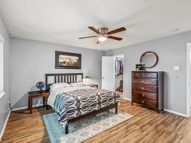 bedroom with baseboards, a walk in closet, wood finished floors, and a closet