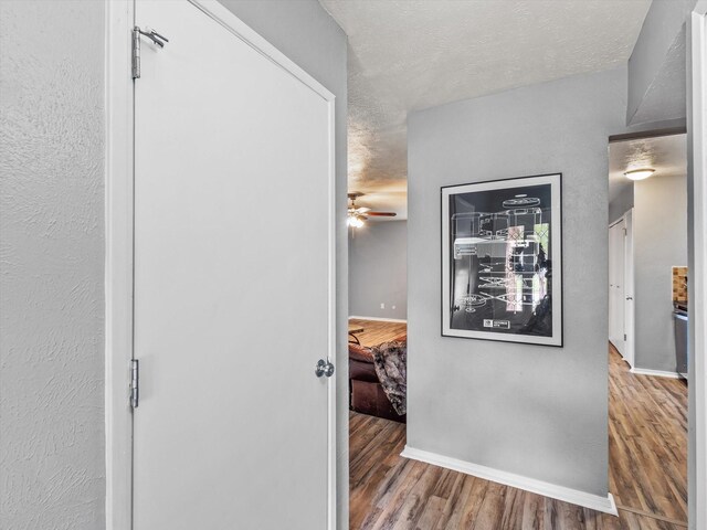 corridor featuring baseboards, a textured ceiling, and wood finished floors