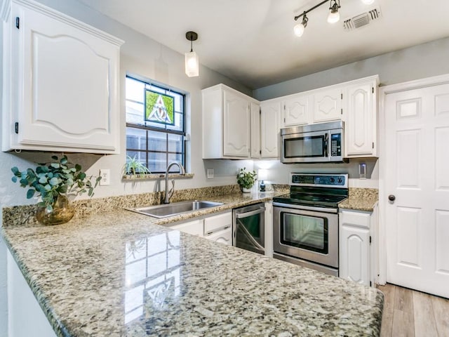 kitchen featuring visible vents, a sink, white cabinets, a peninsula, and stainless steel appliances