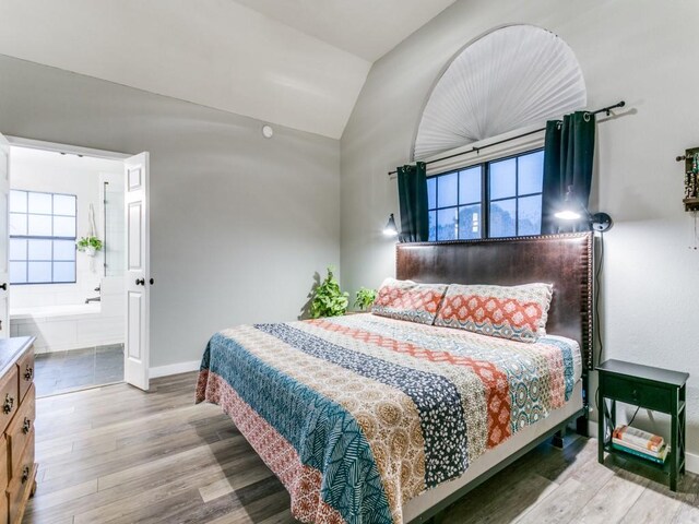 bedroom featuring baseboards, ensuite bathroom, wood finished floors, and vaulted ceiling
