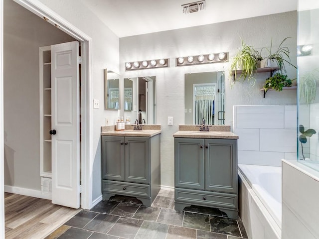 bathroom featuring a bath, visible vents, two vanities, a sink, and a textured wall