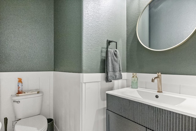 bathroom featuring vanity, a wainscoted wall, and toilet