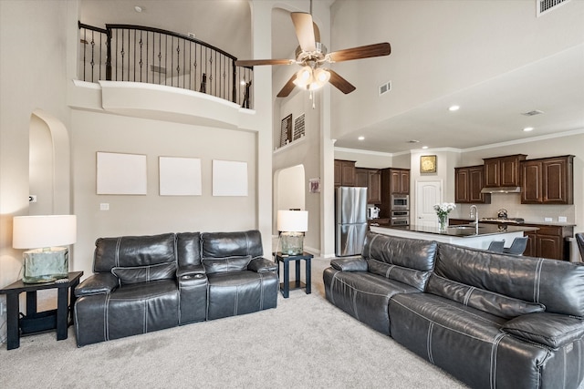 living room with ceiling fan, a high ceiling, light carpet, arched walkways, and visible vents