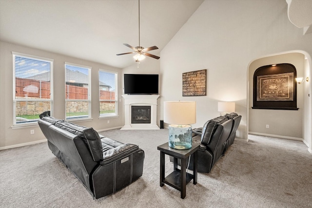 carpeted living area featuring baseboards, ceiling fan, a glass covered fireplace, and a healthy amount of sunlight