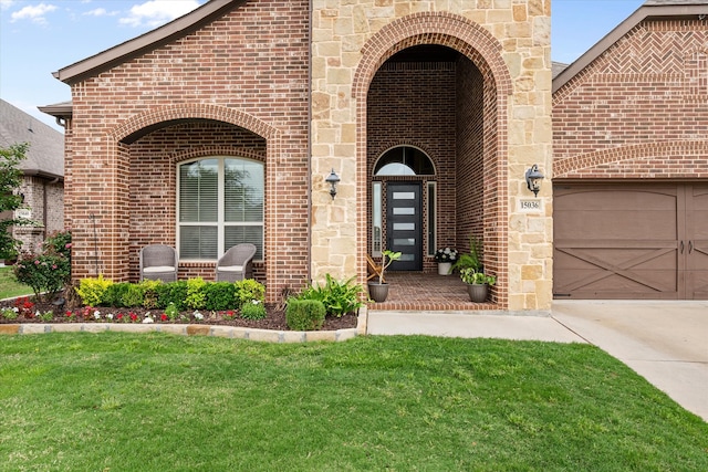 doorway to property featuring a yard, an attached garage, concrete driveway, and brick siding